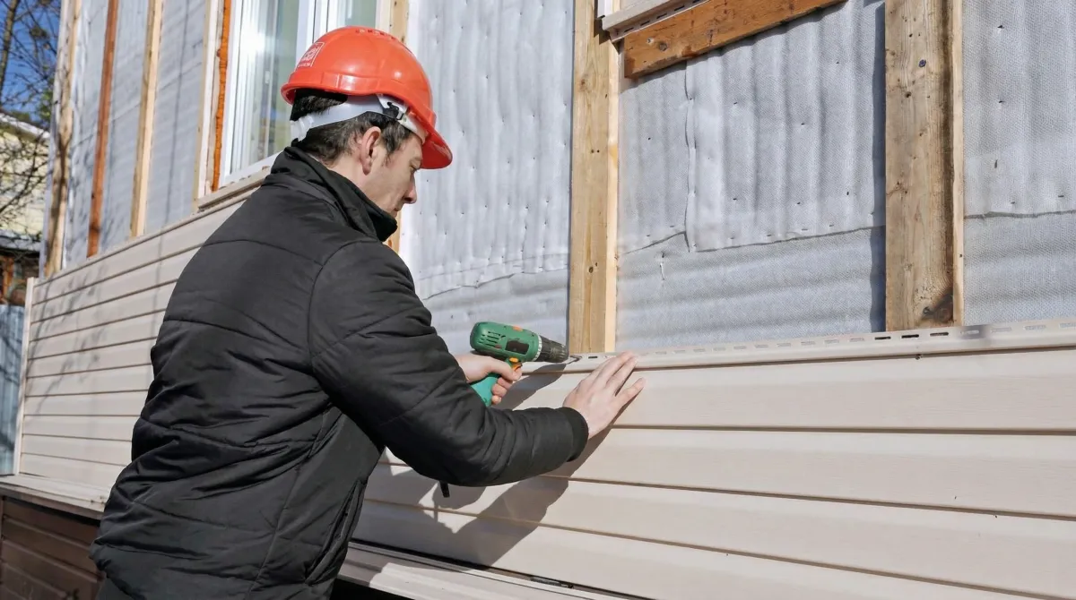 Siding replacement professional using a power drill to install new tan vinyl siding on a home exterior in Louisville, KY